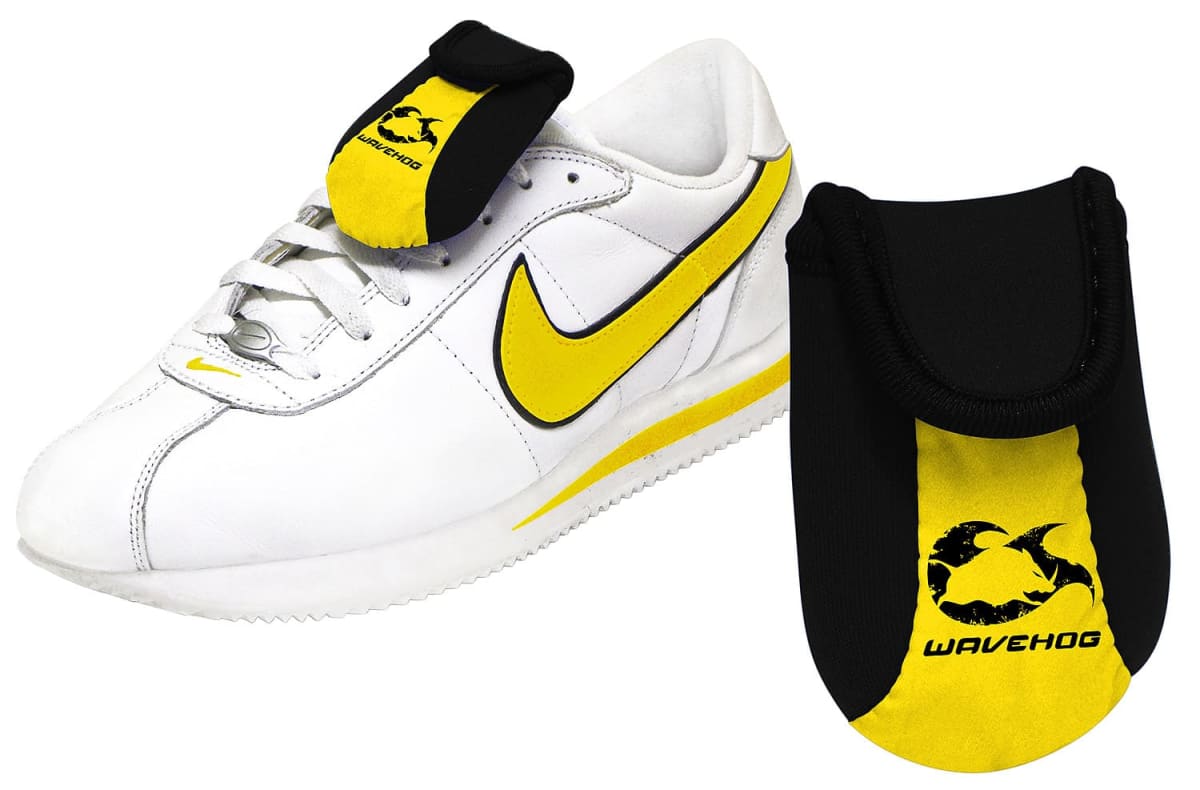 A white sneaker with a yellow swoosh, accompanied by a black and yellow tongue cover labeled Wavehog. The cover protects the shoes laces and is shown separately for detail.