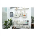 Gray bags with colorful designs are displayed on hooks and a bench in a cozy, plant-filled room.