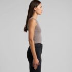 A person with long dark hair stands sideways, wearing a sleeveless gray top and black pants. The background is neutral, highlighting the persons profile.