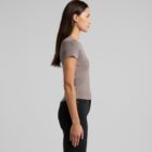 A woman with long brown hair stands in profile against a plain gray background, wearing a taupe short-sleeve top and dark pants.