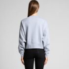 Woman standing with back to camera, wearing a grey sweatshirt and black pants.