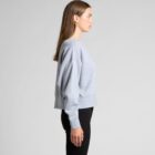 Woman in a gray sweatshirt and black pants standing in profile against a plain background.