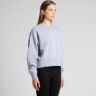 Woman in a light gray sweatshirt and black pants standing against a plain background.