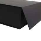 A close-up of an unopened black rectangular box with a sharp, angular design. One end of the box has a triangular flap slightly ajar, revealing the smooth, matte texture of the material.