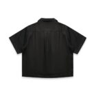 A black, short-sleeved button-up shirt with a boxy fit, viewed from the back. The shirt has a classic collar and a pleat detail under the yoke. The fabric appears smooth and slightly shiny.