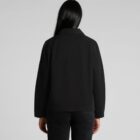 Rear view of a person with long black hair wearing a black jacket and dark pants, standing against a plain gray background.