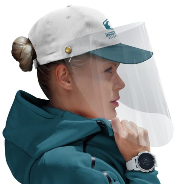 Person in a green jacket and a white cap with a logo, wearing a clear face shield and a white smartwatch. The cap has a teal brim, and the person has their hair in a bun.