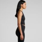 A person with long black hair is standing in profile against a light gray background. They are wearing a fitted black tank top and leggings.