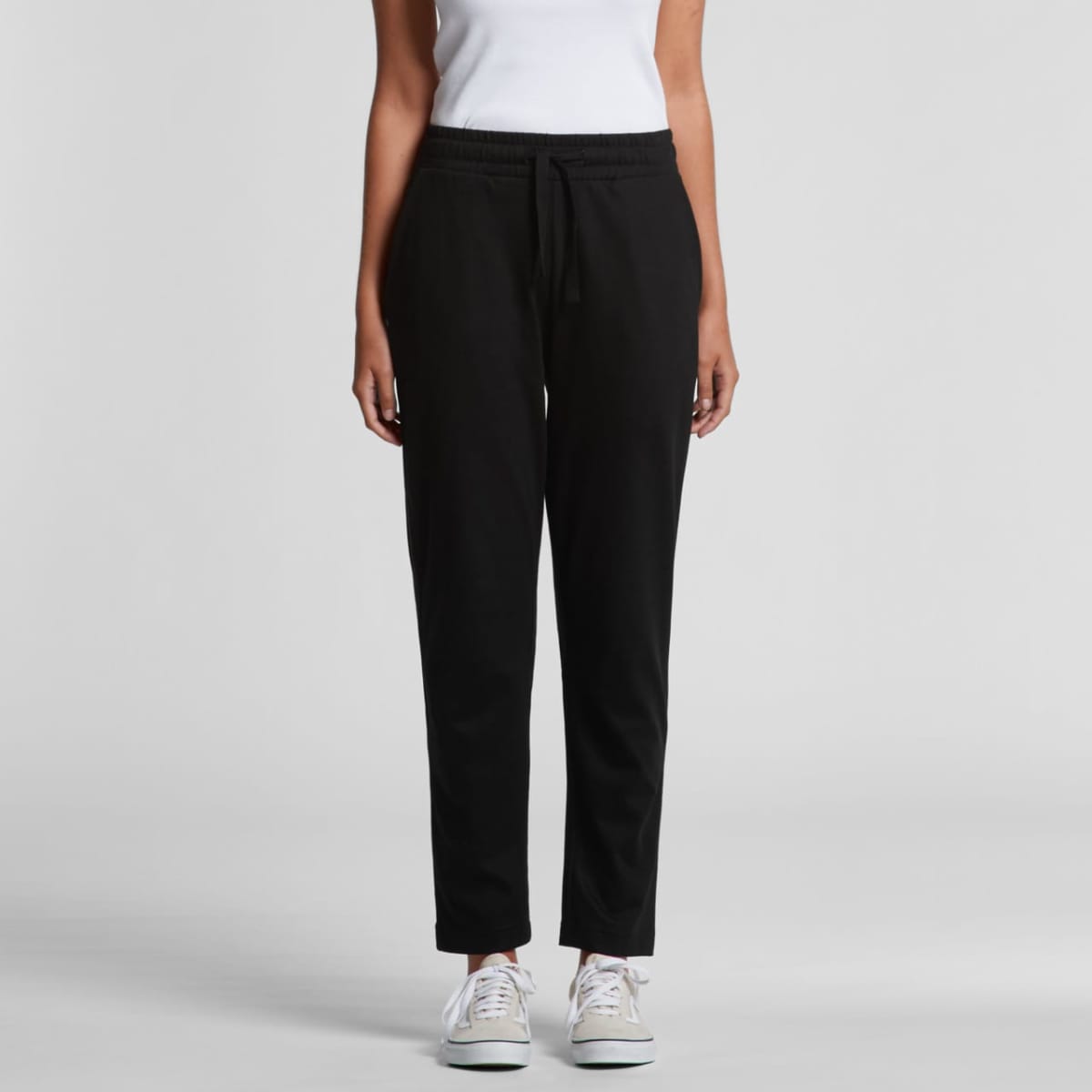A person wearing a white sleeveless top and black jogger pants. They are also wearing white sneakers. The background is plain gray.