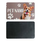 A placemat featuring a smiling corgi with large ears and a text area labeled Pet Name surrounded by white paw prints. The bottom shows the mats plain black underside.