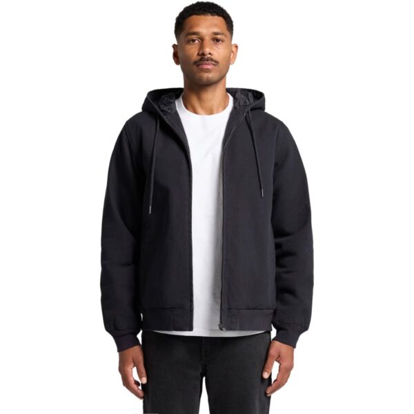 Man wearing a black zip-up hoodie with the hood down, over a white T-shirt and black pants, standing against a plain white background.