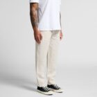 A person wearing a white short-sleeve t-shirt and light beige pants, with black and white sneakers. They have tattooed arms and are standing against a plain white background.