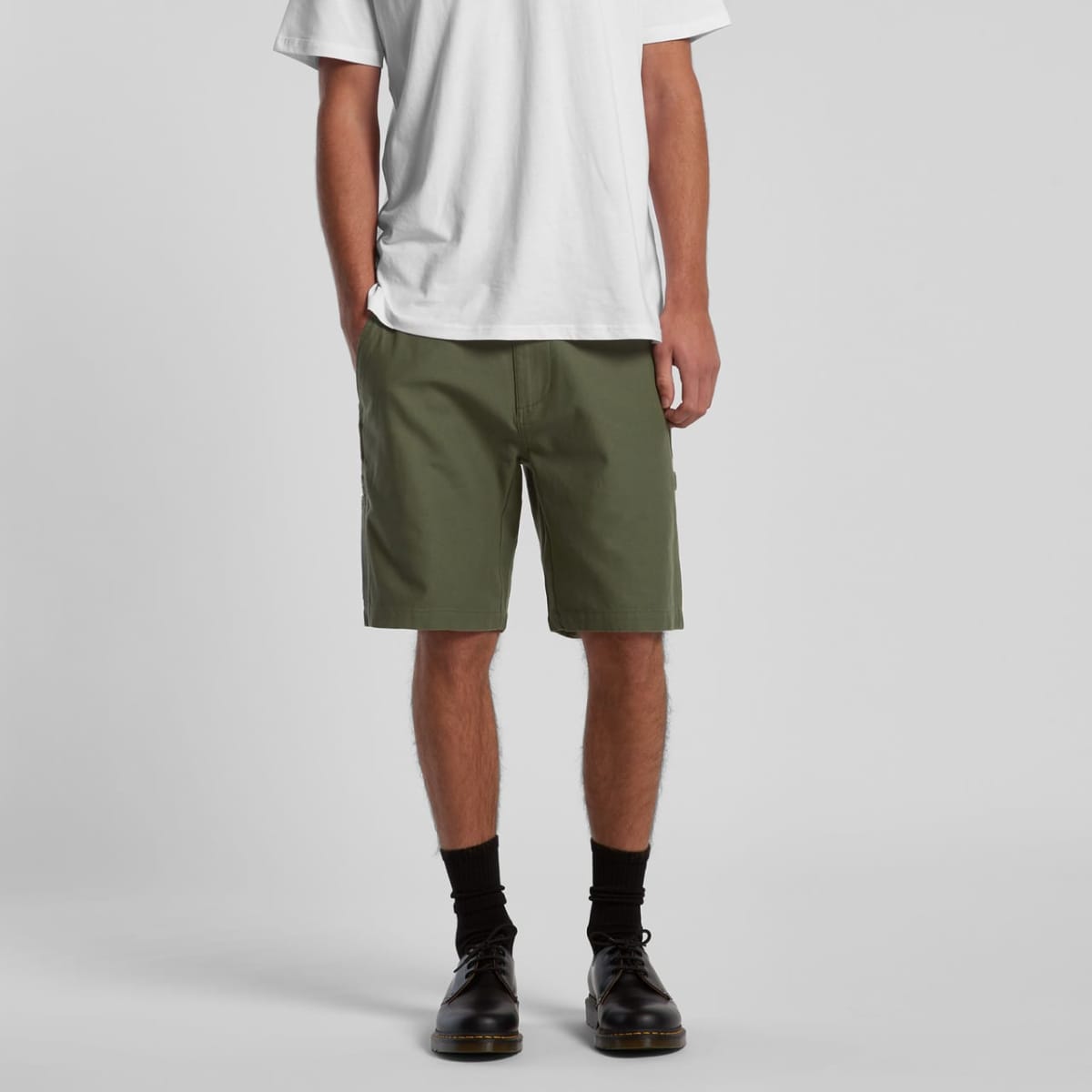A person stands against a plain background wearing a white t-shirt, olive green shorts, black socks, and black shoes. The image focuses on the outfit from the neck down.