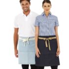 A man and a woman stand side by side, both wearing aprons. The man is in a white polo and light blue apron, while the woman wears a checkered shirt and dark blue apron. Both smile at the camera against a white background.