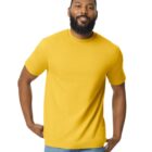 A man with a beard is smiling and wearing a bright yellow T-shirt and blue jeans. He stands against a plain white background, with his left hand in his pocket and his right hand resting on his hip.