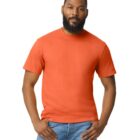A man with a beard wearing an orange T-shirt and blue jeans stands against a plain white background. His hands rest on his hips, and he faces the camera directly.
