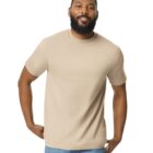 A man with a beard is smiling while wearing a plain beige T-shirt and blue jeans. He stands against a white background with his hands resting on his hips.