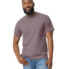 A person with a beard and short hair smiles, wearing a gray t-shirt and blue jeans. The background is plain white.