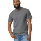 A person with a beard is smiling and standing against a plain white background. They are wearing a gray T-shirt and blue jeans.