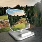 A smartphone stand displays a scenic photo of a lush golf course with green fairways, trees, and a partly cloudy sky. The stand has a sleek white design and is set on a gray surface.