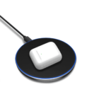 A wireless charging pad with a white charging case placed on it. The pad is round, black, with a thin blue LED light around its edge, and is connected to a power cable. The case has a small green indicator light.