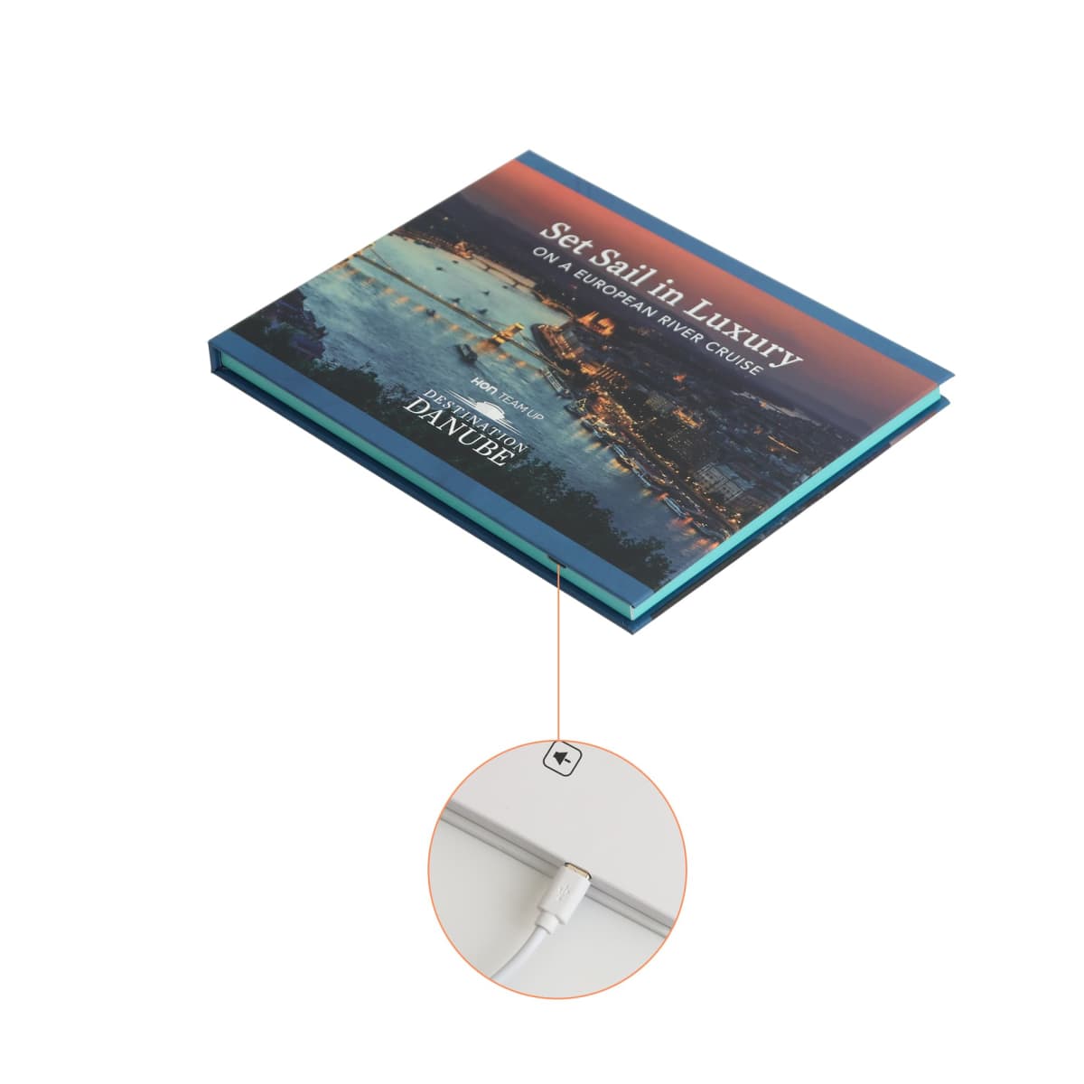 A cruise brochure with a cover photo of a scenic night view of a river and city lights. The brochure is displayed with an illustration highlighting a charging port on its spine.