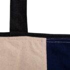 Close-up of a canvas tote bag showing the top corner. The bag features two sections, one in beige and the other in dark blue, with a black fabric handle attached at the top. The stitching along the seams is visible.