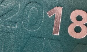 Close-up of 2018 embossed on a textured teal surface, reminiscent of an AU Felt Shoppers elegant design. The 1 is highlighted in reflective silver, adding sophistication to the scene.