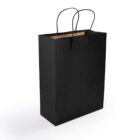 A black paper shopping bag with black handles is standing upright against a white background. Its top is open, revealing a brown interior. The bag is positioned slightly to the right.