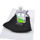 A bottle of hand sanitizer labeled Pullman Pharmacies is placed on top of a black face mask with Pullman Pharmacies printed on it. The items are on a white transparent pouch.