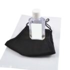 A small bottle of clear hand sanitizer rests on top of a folded black face mask, both placed on a white surface. The bottle has a white cap and a blank label.