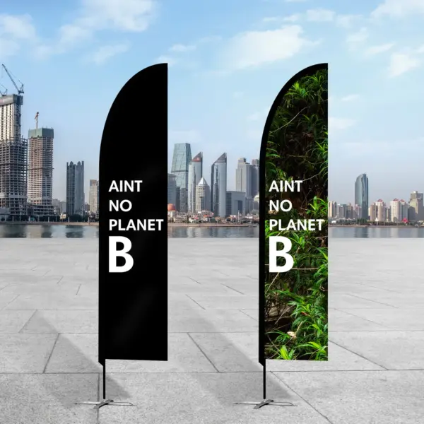 Two vertical banners stand on a paved surface with a city skyline backdrop. Both feature Aint No Planet B in white text. The left banner is solid black, while the right displays a vibrant green leafy design on the eco-friendly VibrantEco rPET Feather Banner - Large.