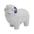 A small, white ceramic sheep figurine with textured fur and blue-tipped spiral horns stands facing the right. The figurine features simple painted eyes and a red-lined mouth, set against a plain white background.