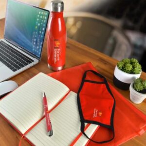 Laptop, water bottle, notebook, pen, and a hint of fortune cookies on a wooden desk.