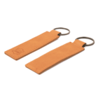 Two tan leather keychains with rectangular tags and metal rings are displayed side by side. The left keychain features a debossed logo of a leather symbol. Both have a simple and elegant design.