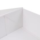 A close-up view of the corner of a white triangular box. The smooth surfaces converge at a right angle, highlighting the clean lines and minimalistic design of the box.