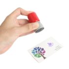 A hand holds a red and gray stamp above a white card with a colorful tree design and a purple logo. The card features the word QUEEN.

.