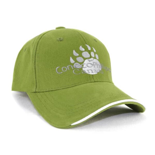 A green baseball cap featuring a white paw print design with the text Concordia Canada embroidered on the front. The cap has a curved brim with a white accent along the edge.