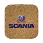 A square cork coaster featuring the Scania logo, which includes a stylized griffin head above the word SCANIA in blue text on a light brown background.