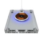 A transparent, rectangular wireless charger with a visible copper coil glows blue. It has a connecting white cable and is set against a white background.