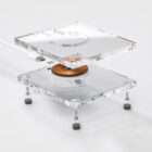 A transparent, modular wireless charging pad is shown disassembled, revealing its internal components, including copper coils and circuit boards, against a plain white background.