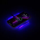 A smartphone displaying 11:45 and 50% charged is wirelessly charging on a glowing purple and blue charging pad in a dark setting.