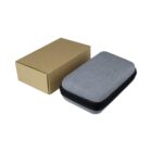 A gray, zippered fabric case next to a plain cardboard box. The case is rectangular with rounded edges and appears compact and portable.