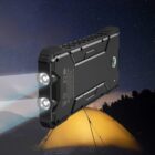 A rugged power bank with dual LED flashlights and a built-in compass is shown illuminating a dark outdoor scene. A glowing tent and a starry night sky provide a scenic backdrop.