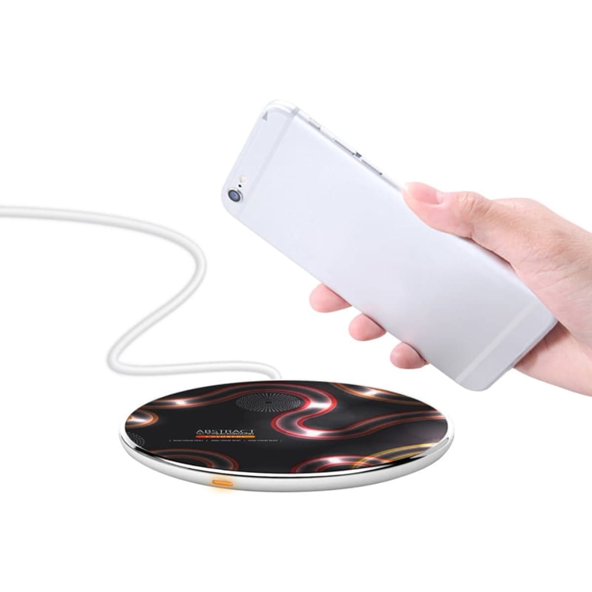 A hand holding a smartphone, hovering over a stylish circular wireless charger with a swirled black, red, and white design. The charger is connected via a cable, suggesting functionality.