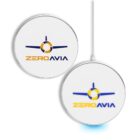 Two white circular wireless chargers with the ZeroAvia logo, featuring a stylized airplane and the text ZEROAVIA in blue and orange. One charger has a connected cable and emits a blue light at the base.