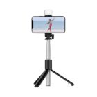 A smartphone mounted on a black tripod is displaying a photo of a person jumping on a beach. A small light is attached on top of the phone. The tripod has three extended legs for stability.