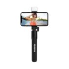 A smartphone mounted on a black selfie stick labeled REUNION with an LED light on top. The phone displays a woman outdoors, smiling and taking a selfie.
