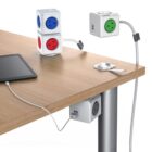 A wooden table with modular power cubes attached. One cube is mounted on the table leg with USB ports, while others are on the tabletop. A tablet is connected via a charging cable to one of the cubes.