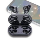 A set of black wireless earbuds with an ergonomic design displayed alongside their open charging case. A blurred image of a smartphone with a call interface is seen in the background.